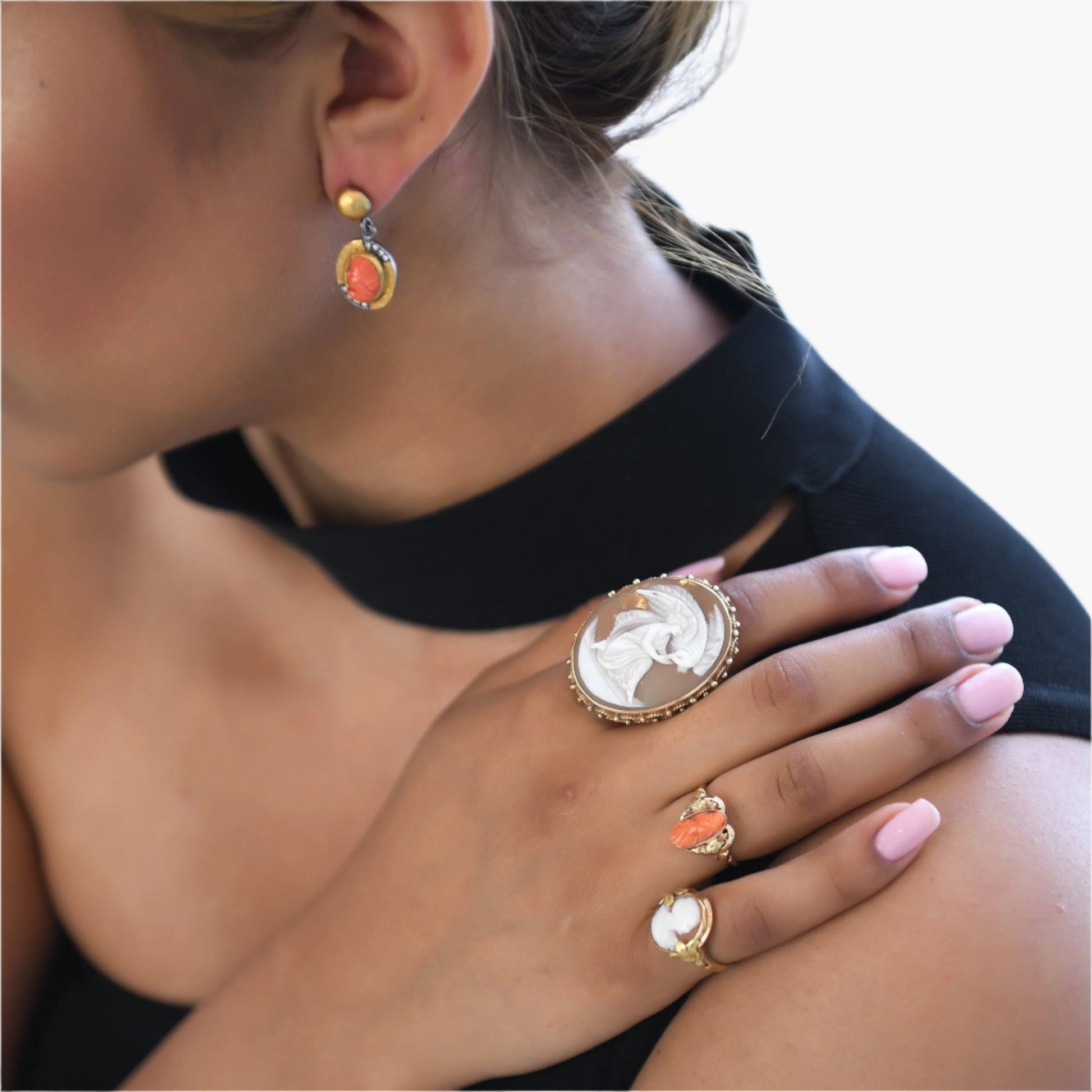 Model wearing (left to right) Natural Coral,  24 karat gold earrings from Turkey, Large cameo shell ring featuring Leda from Greek mythology who was seduced by Zeus when he takes on the form of a swan. She was a queen of Sparta who was mother of beautiful Helen who sparked the Trojan War in 14 karat yellow gold.  Antique coral cameo (left facing) ring and last, Deco style (left facing) natural shell cameo ring.  